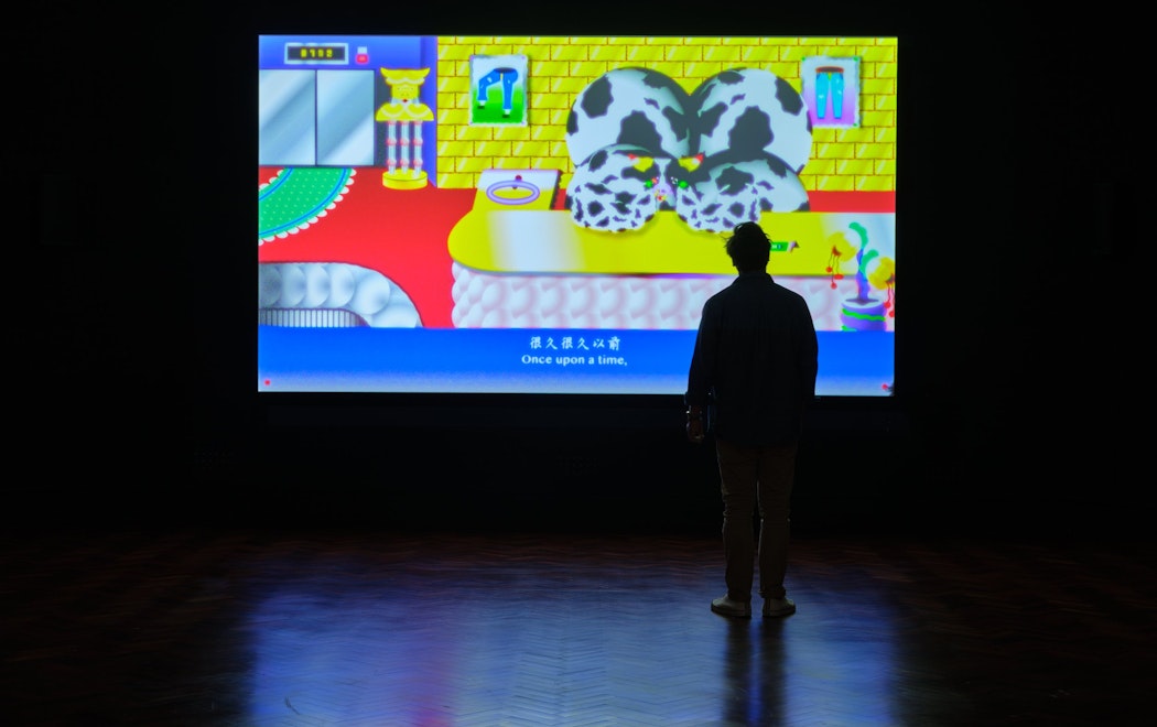 A silhouette stands near a large screen playing the work of Wong Ping