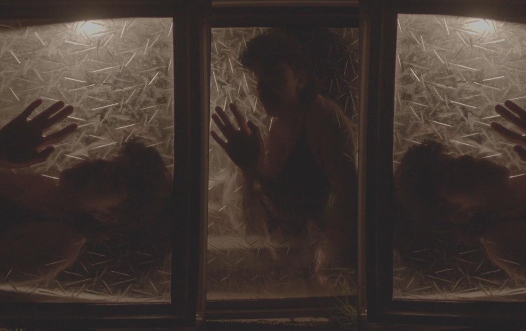 Behind three panels of frosted glass we see three separate shots of the same person with their hand pressed to the glass. Their face is in shadow.