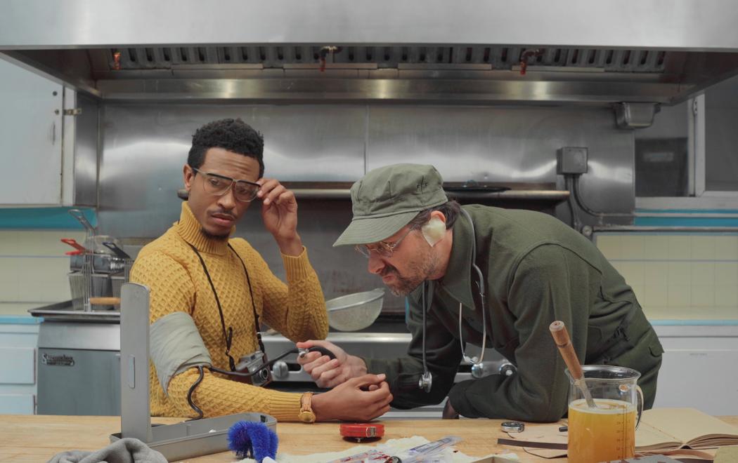 Two men in a kitchen perform vaguely medical or scientific actions
