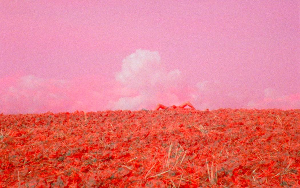 A shot of a hilltop awash in saturated red and pink. At the top appears to be the limbs of a human.