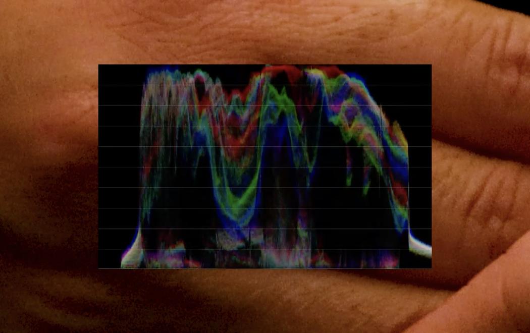 A colourful digital wave form is overlaid on a hand, two types of imagery brought together in one frame, one abstract data, the other photo realistic.