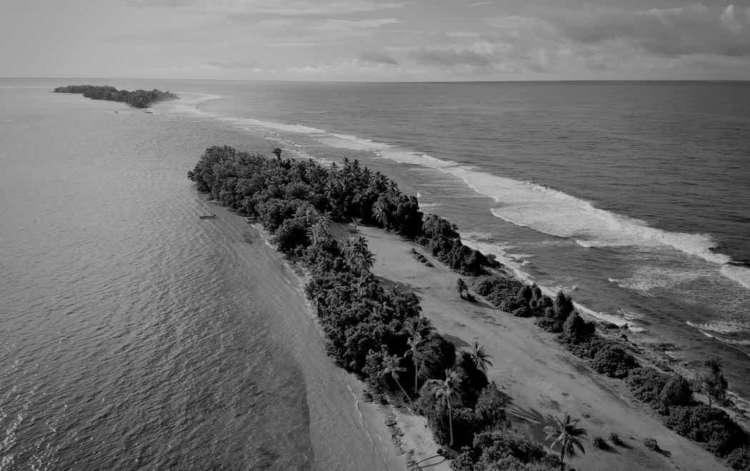 Black and white aerial footage of a Pacific island surrounded by ocean