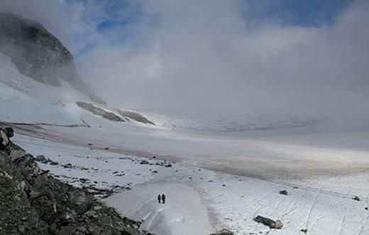 Taken from high up this image shows two people who are small in the distance standing upon icy landscape, in front of them is icy wind