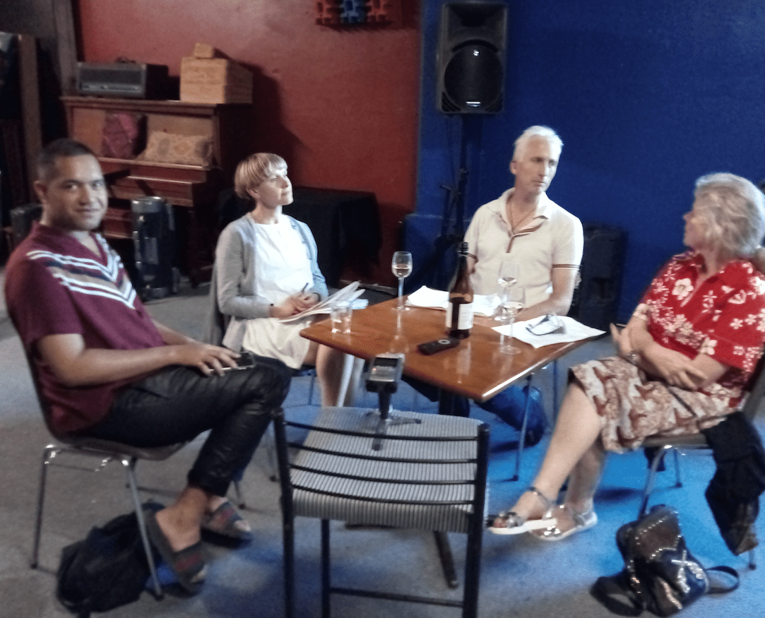 Four people sit around a small table having a discussion. There is a bottle of wine on the table as if they have been drinking whilst talking.