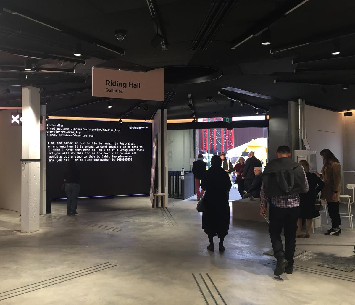 People move through a gallery space with concrete floors. Signage reads "riding hall galleries"