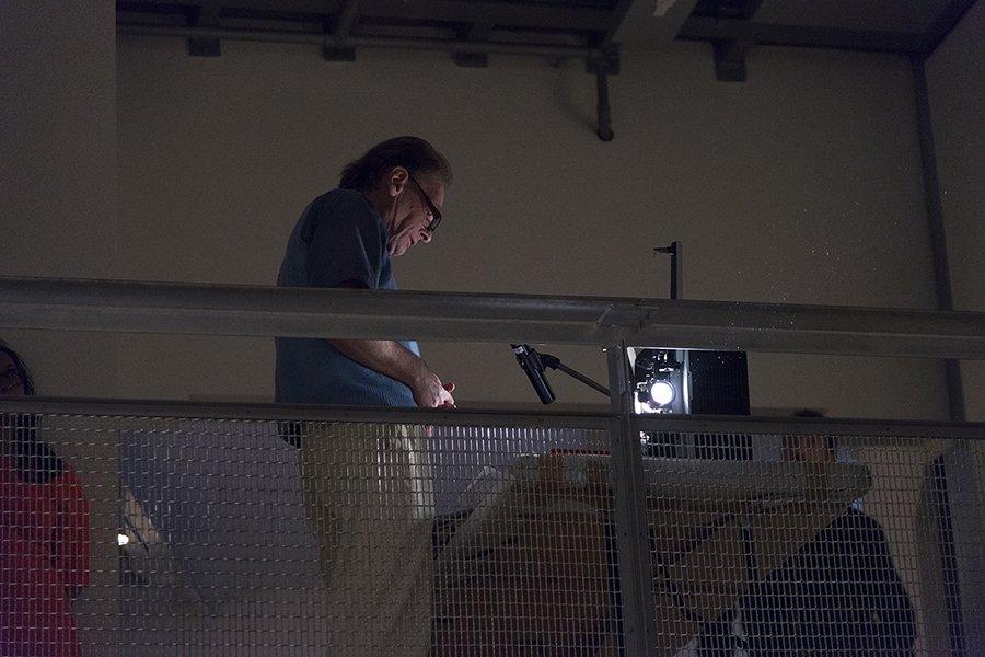 Film-maker Martin Rumsby stands next to a 16mm projector, reading a script into a microphone