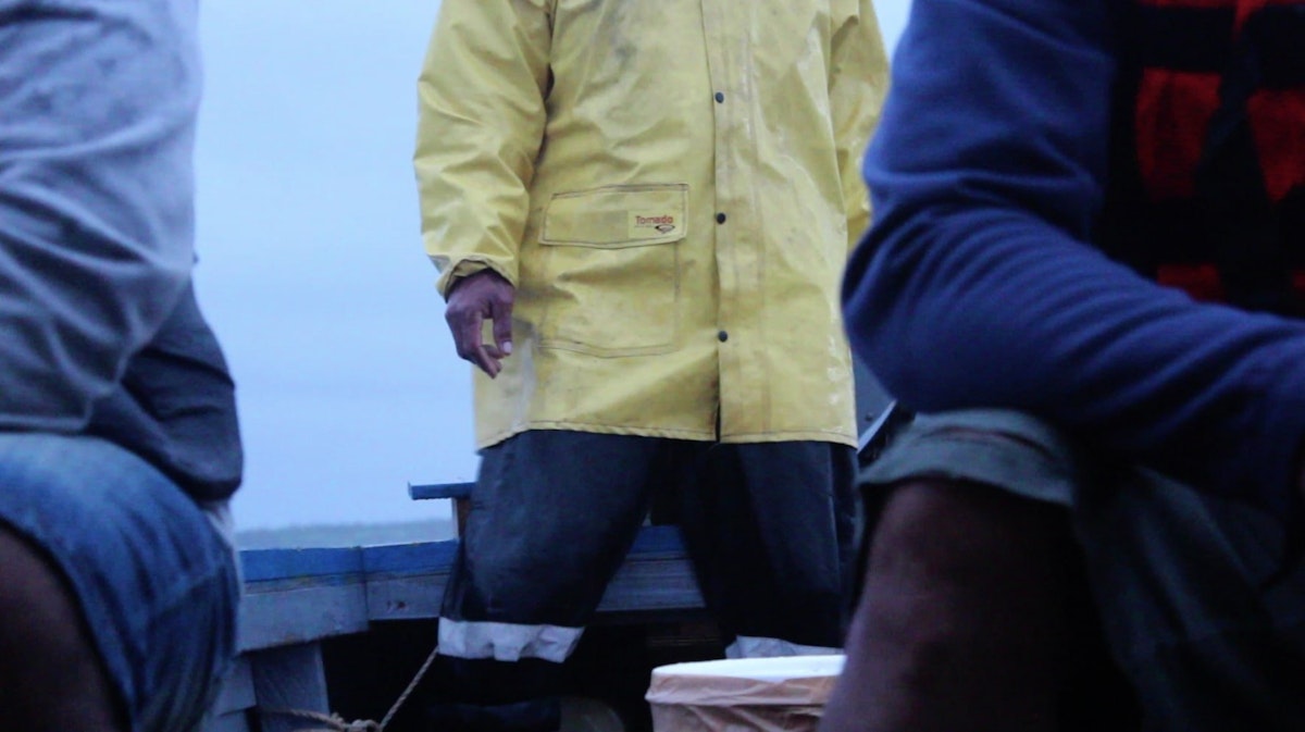 A sailor wearing oilskins stands in the stern of a small boat