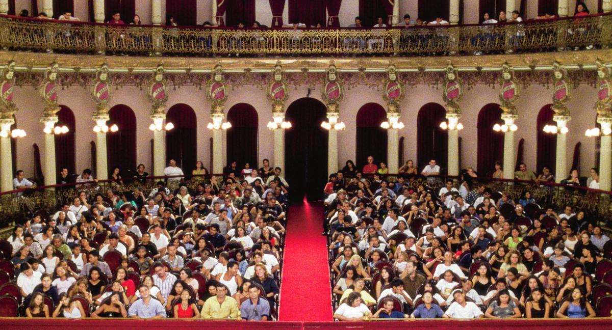 A fancy baroque cinema backed with people who look very bored or tired