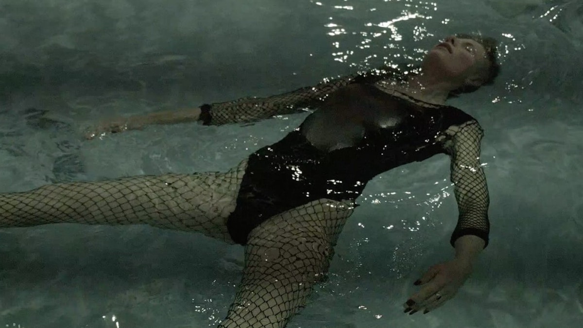 A person wearing tights and swimming costume lies on their back in a pool, eyes closed