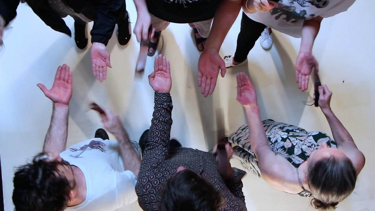 Six people play a musical game, hitting each other with leather belts whilst facing each other