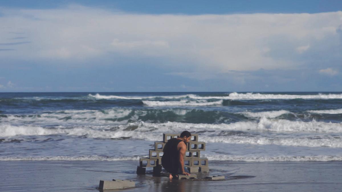 A person builds a wall from concrete bricks on the wet sand as the waves crash near by