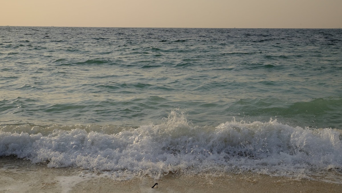 Small blue waves crash against a golden sandy beach
