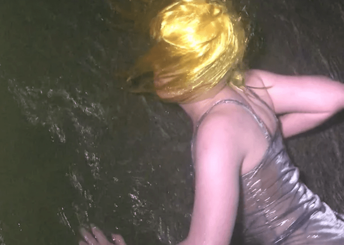 Aliyah crawls along a wet rock at Island Bay beach in the dark wearing a fluorescent yellow wig.