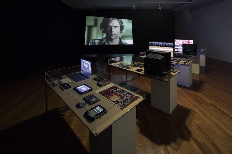 Museum-esque display of objects and monitors inside glass vitrines