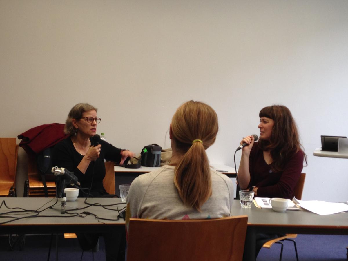 Three people sit around a table in discussion holding microphones