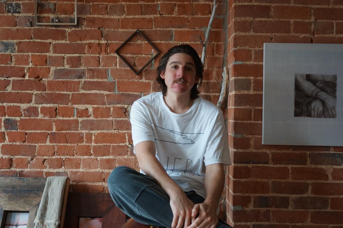 John Ward Knox sitting on a stool in their brick walled studio