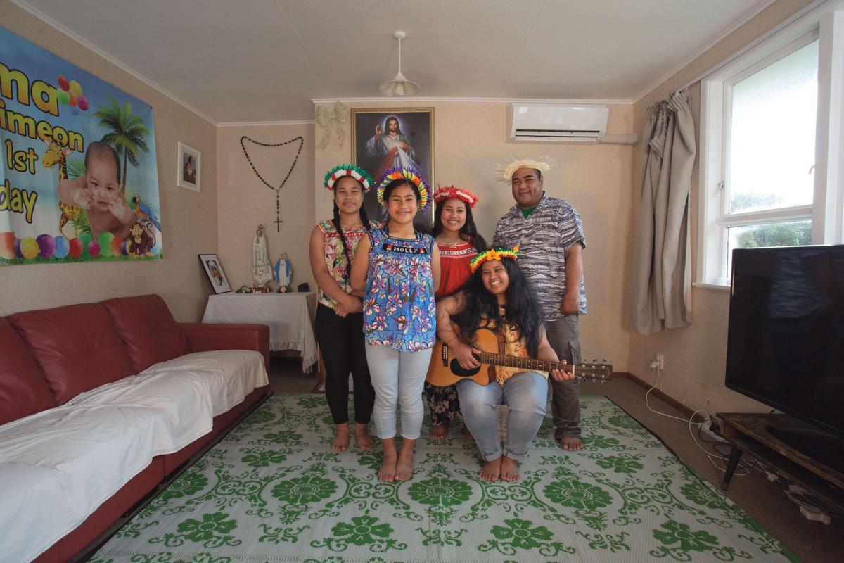 Four people stand together in a colourful lounge smiling brightly wearing pasifika headdress