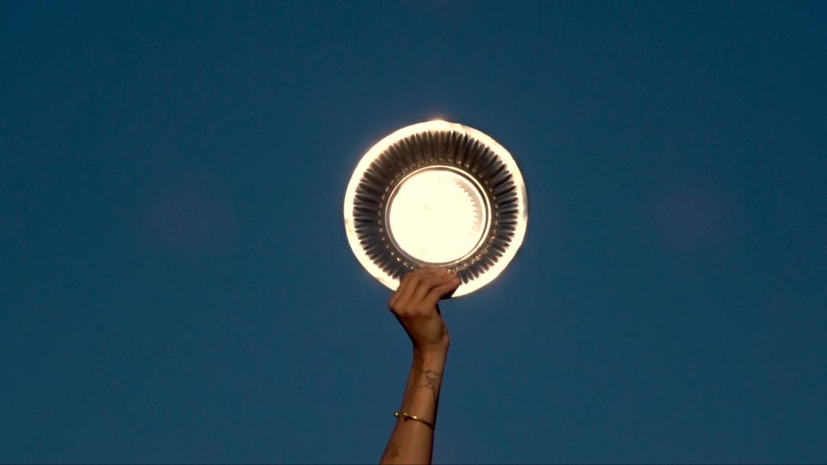 A hand holds a gold charger plate up against a bright blue sky