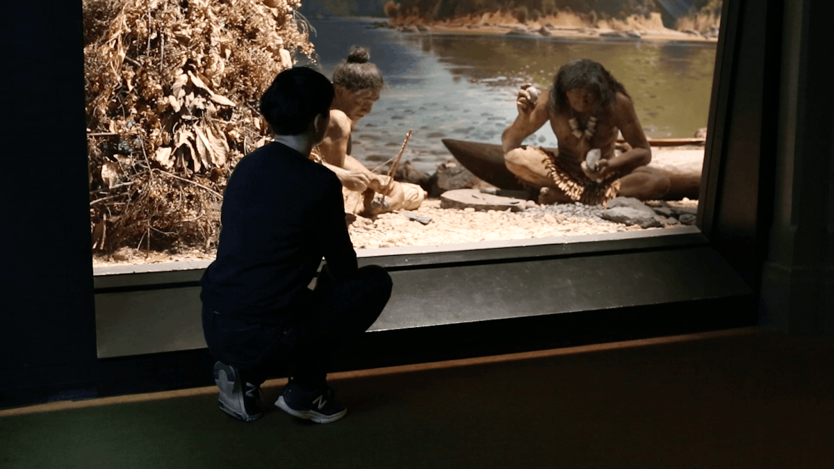 Ana squats down in a museum to haze upon a racist exhibit of Māori people in a museum