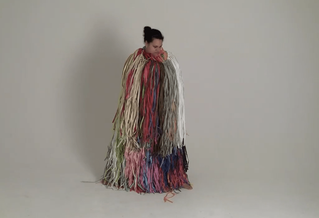 Darcel stands in a white raffia costume against a plain white background