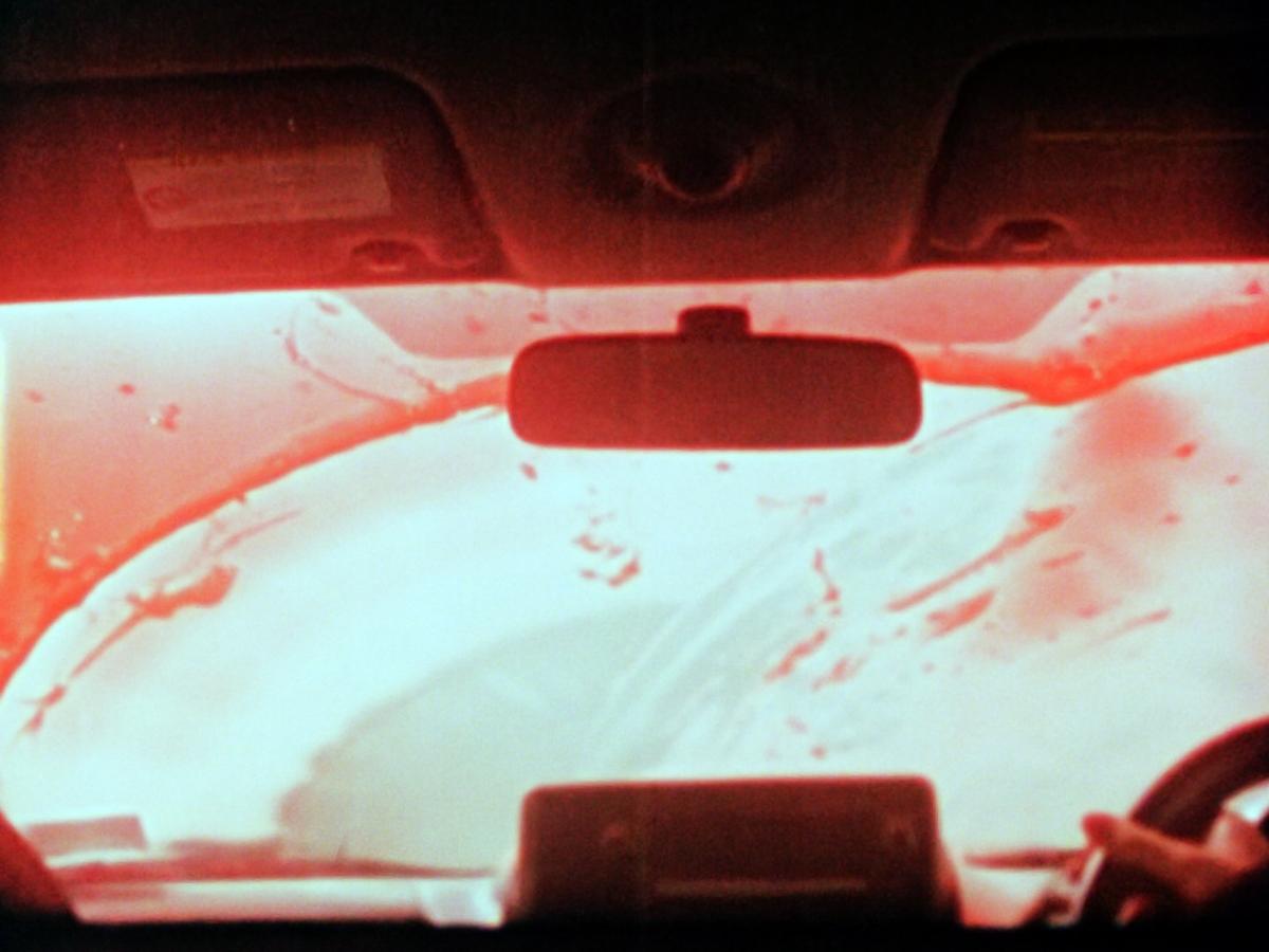 Red liquid or blood is wiped from a car windscreen, seen from inside the car