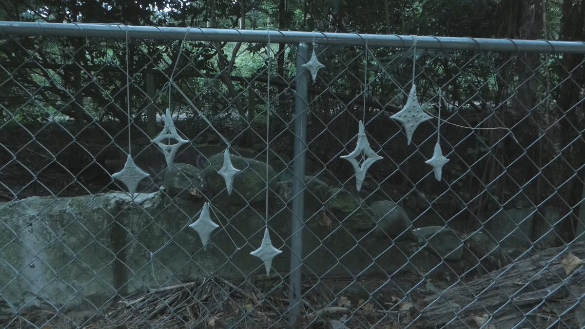 A cluster of nine handmade stars (representing Matariki) hang from a chain link fence.