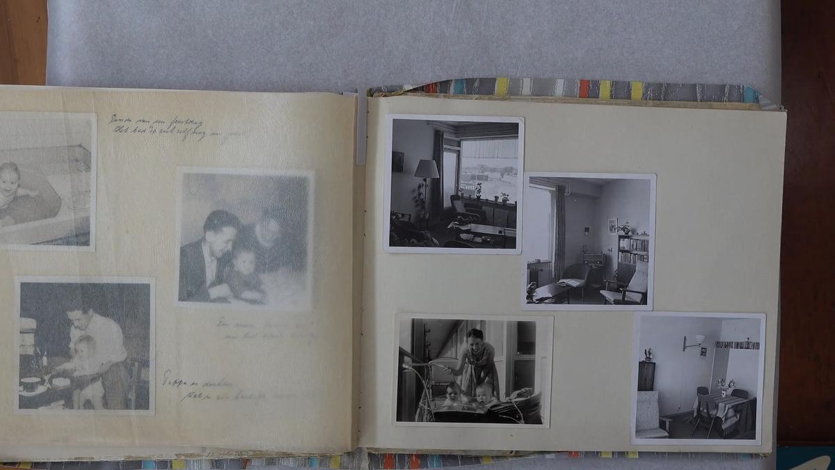A family photo album is open on a table. The photos are black-and-white and depict domestic interiors alongside scenes of family life.