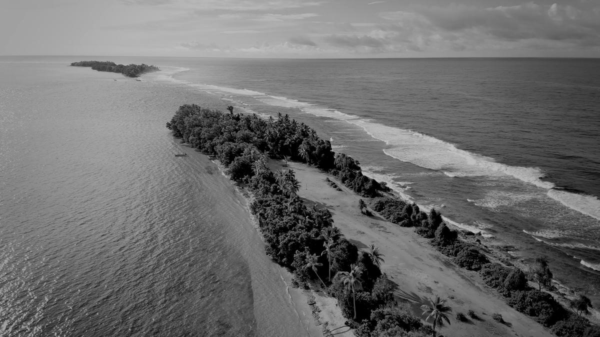 Black and white aerial footage of a Pacific island surrounded by ocean