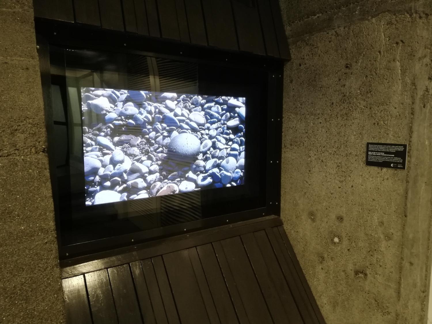 An image of rocks on a shoreline shows on atv screen set into a wall in an industrial public space