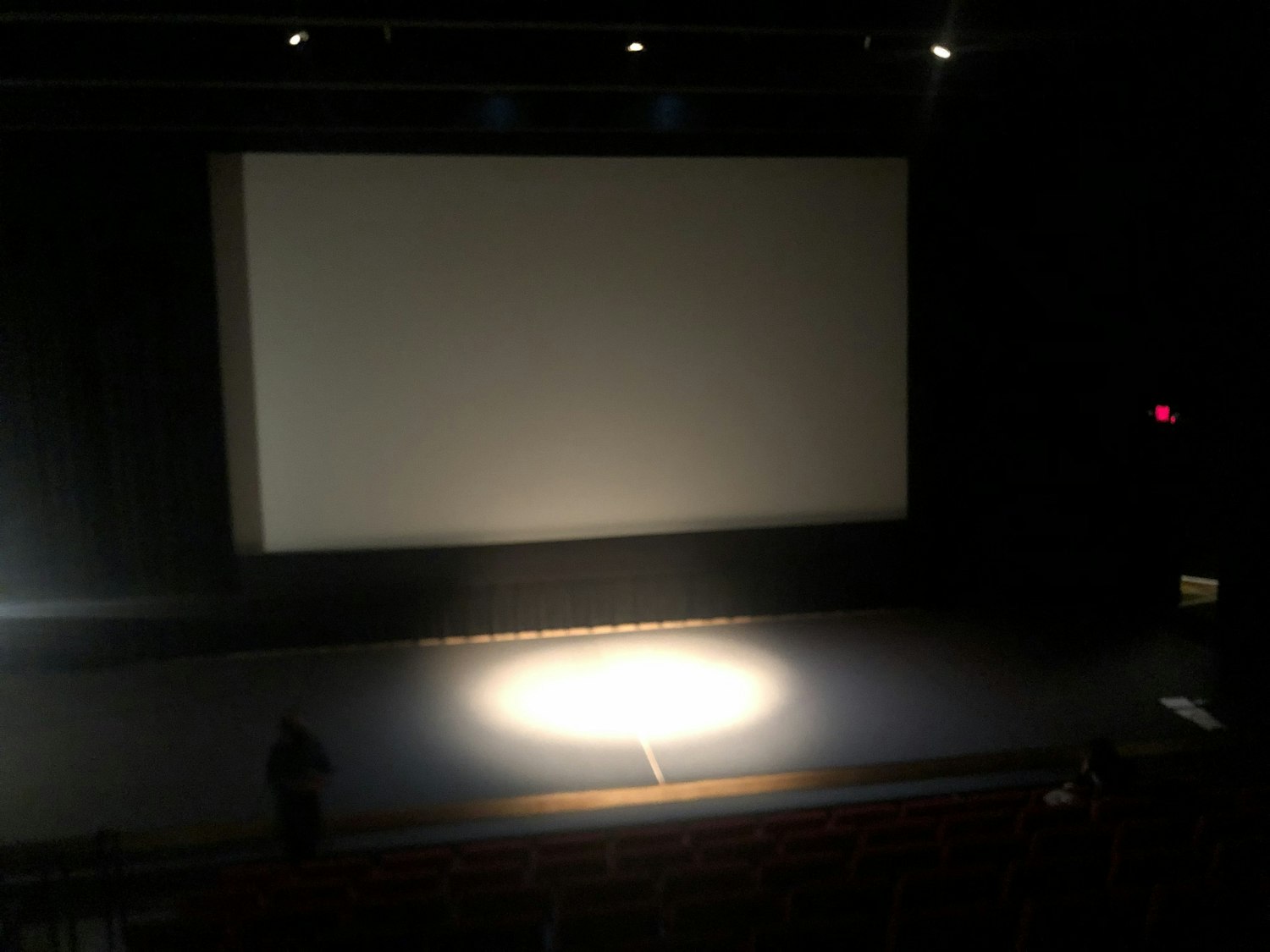 A darkened screen is mounted behind a stage with a spotlight
