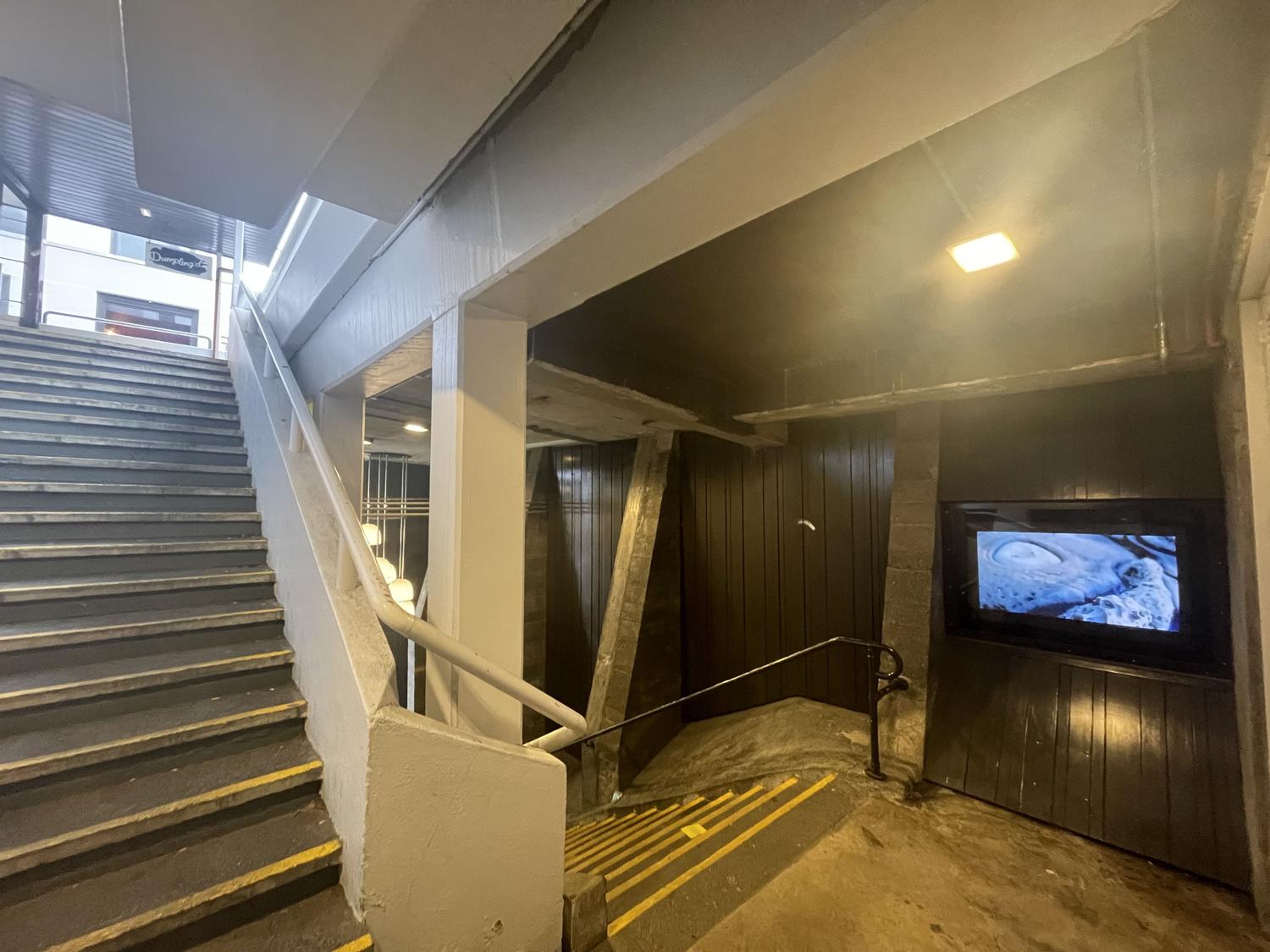 A stairwell with the Masons Screen public art video monitor displaying an image of a rock form by Phil Dadson