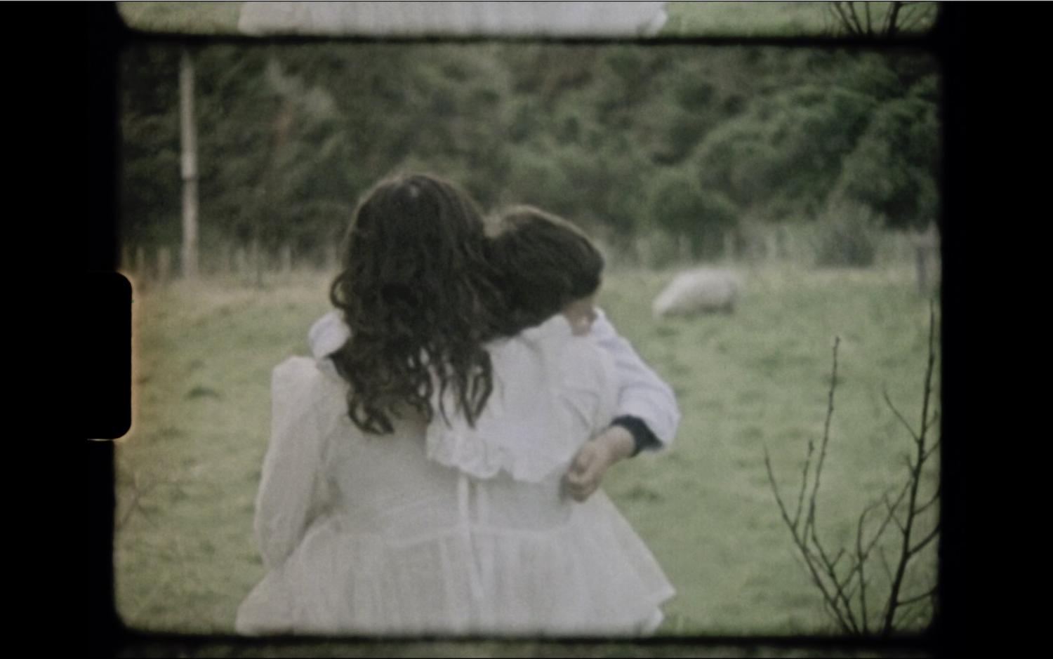 A mother carries a child through a field.