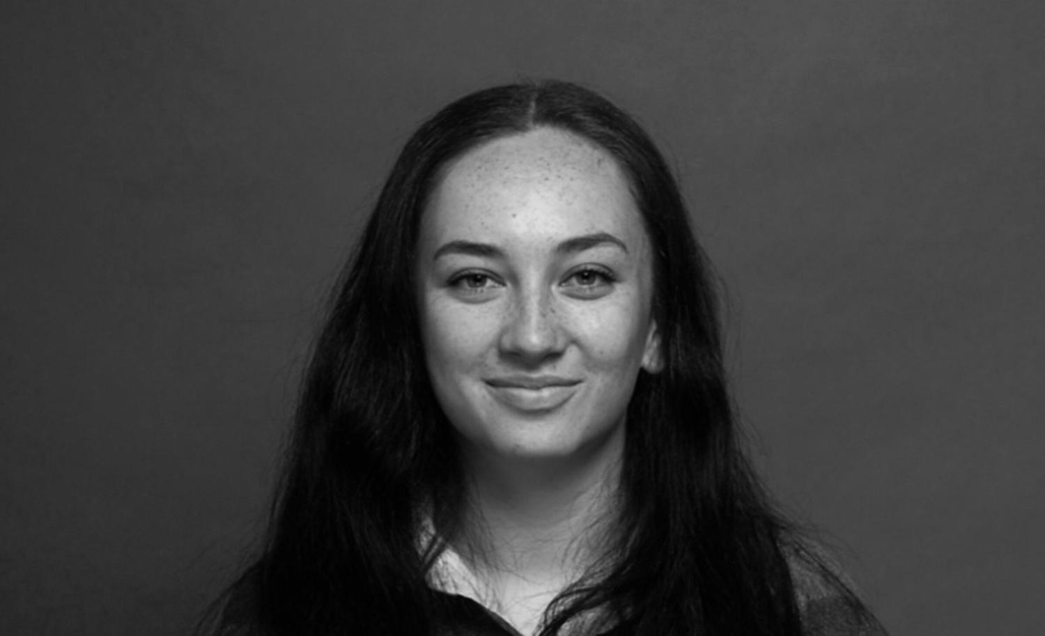 A young woman smiles at the camera. Her hair falls on her shoulders.