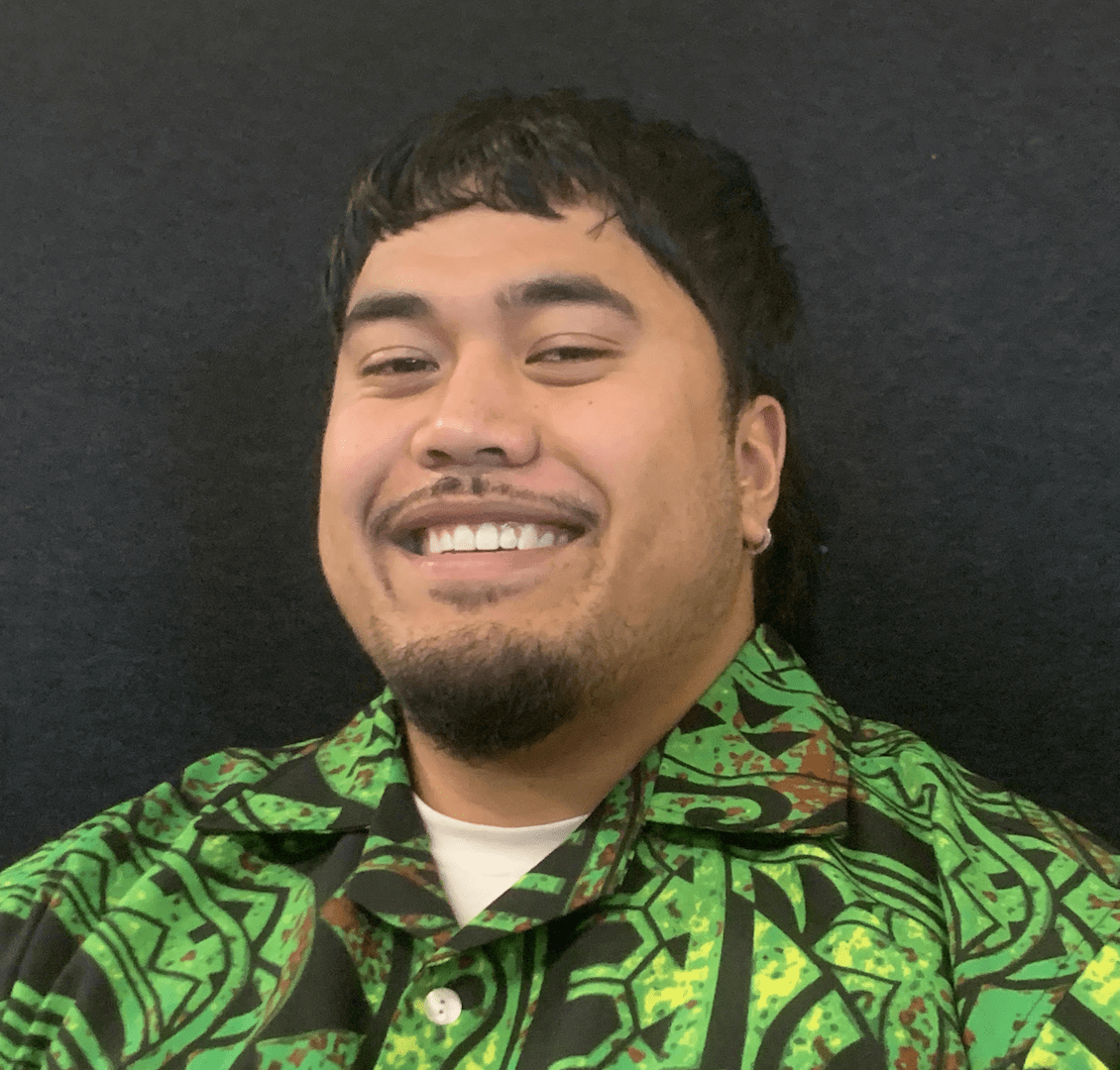 A man smiles at the camera, he is wearing a bright green shirt