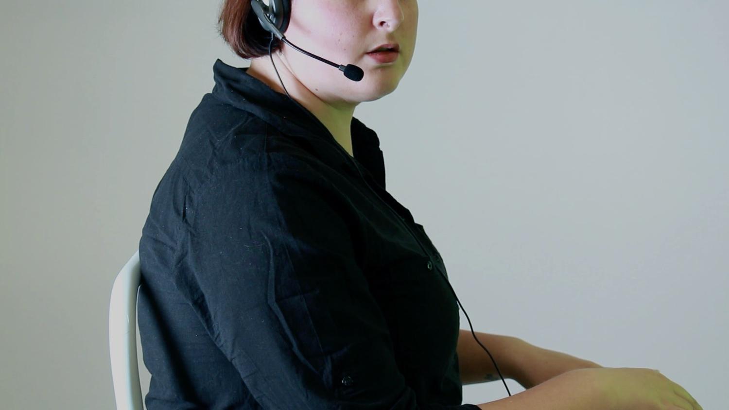 A person wearing a call centre headset and appearing to type at a keyboard turns their head to the right, as if suddenly having their attention drawn elsewhere.