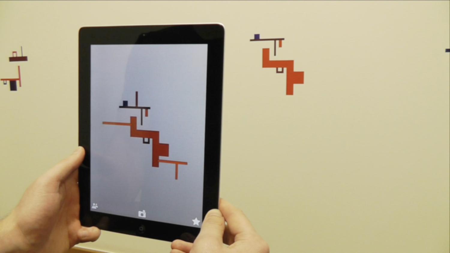 A person holds up a tablet in front of a geometric shape on the wall. Through the video screen the geometric shape is embellished with extra design elements