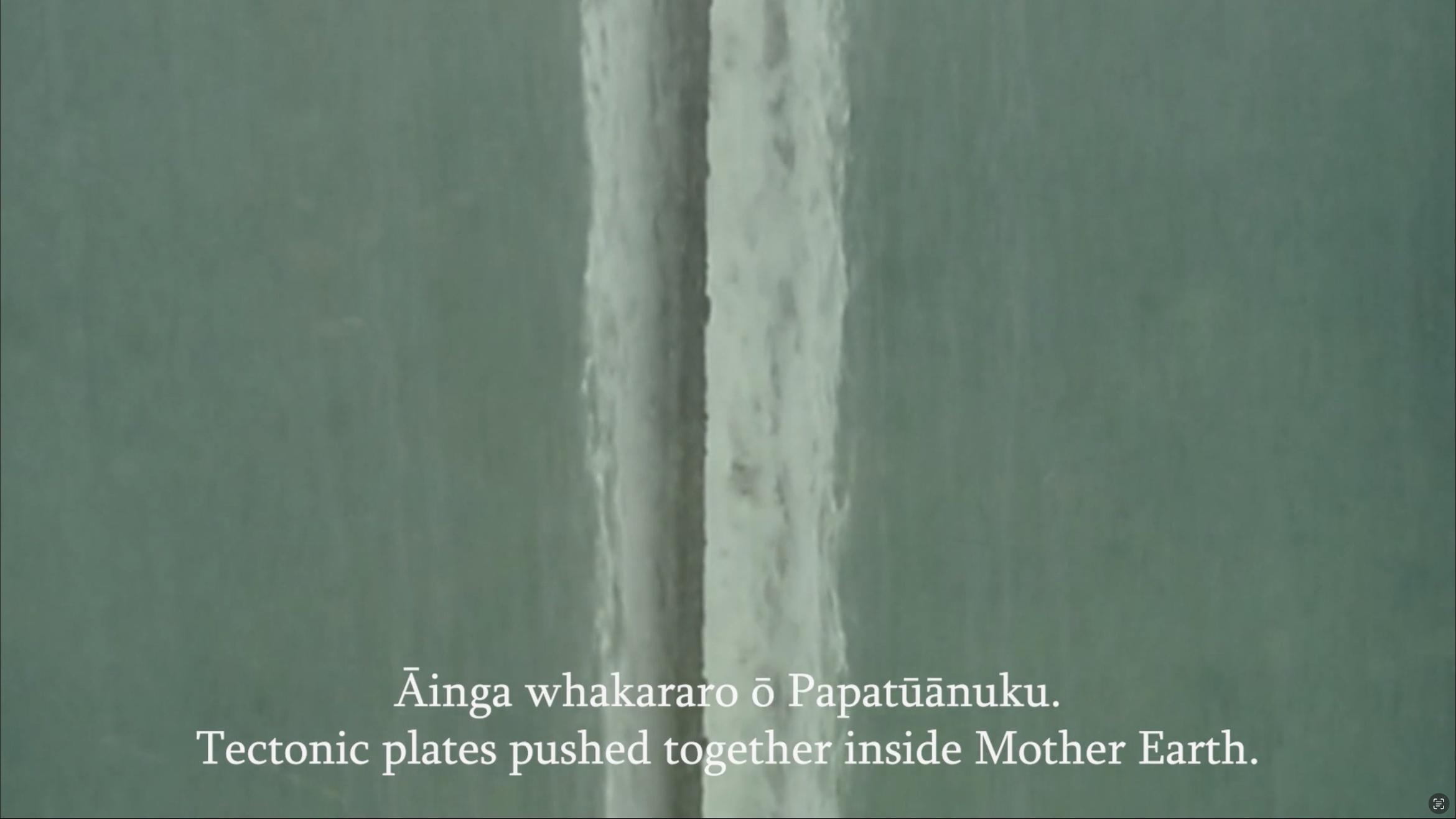 A view of water is overlaid with a bilingual subtitle in te reo and English, this reads 'Tectonic plates pushed inside Mother Earth'