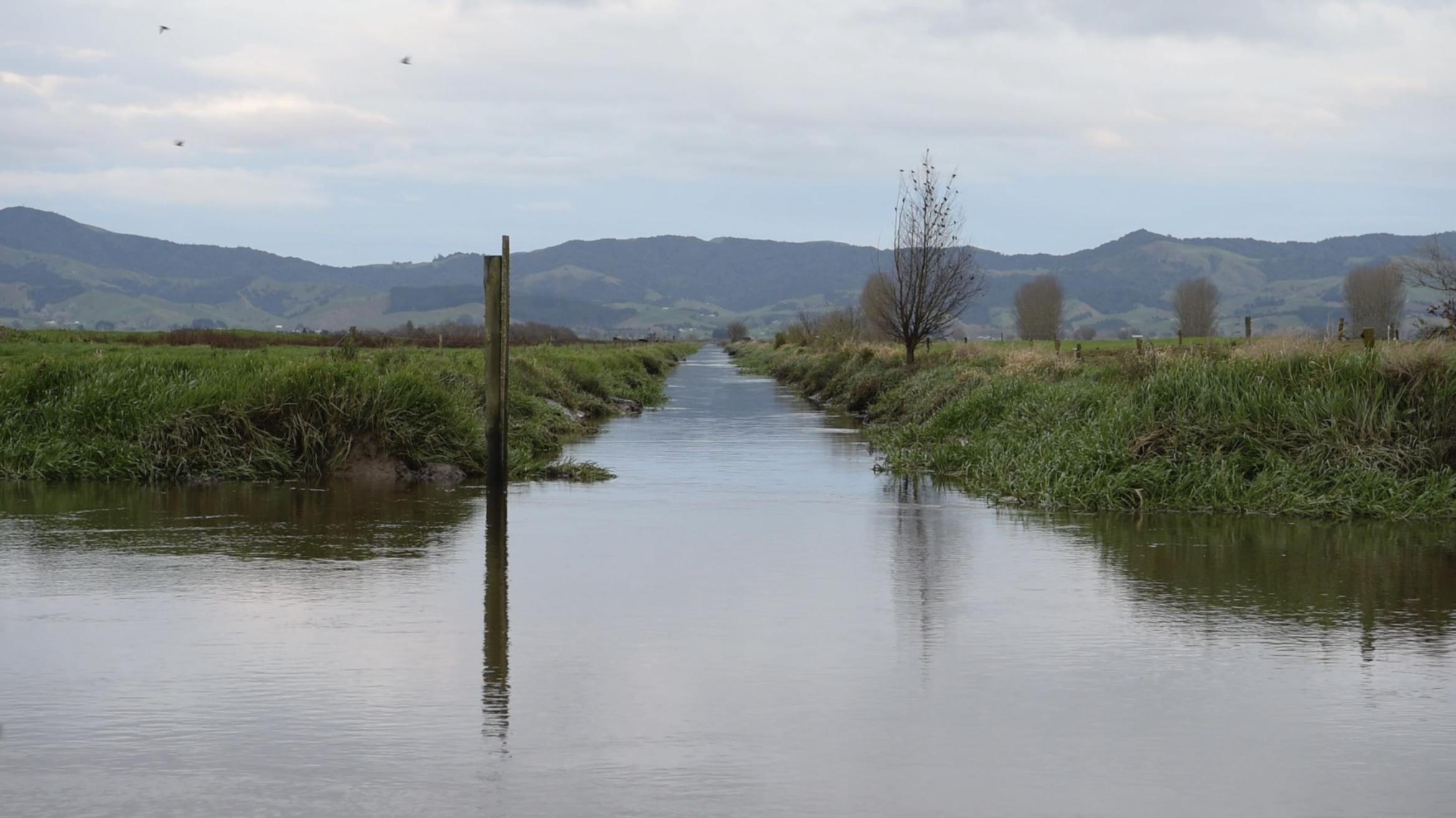 An artificially made waterway bisects a green field.