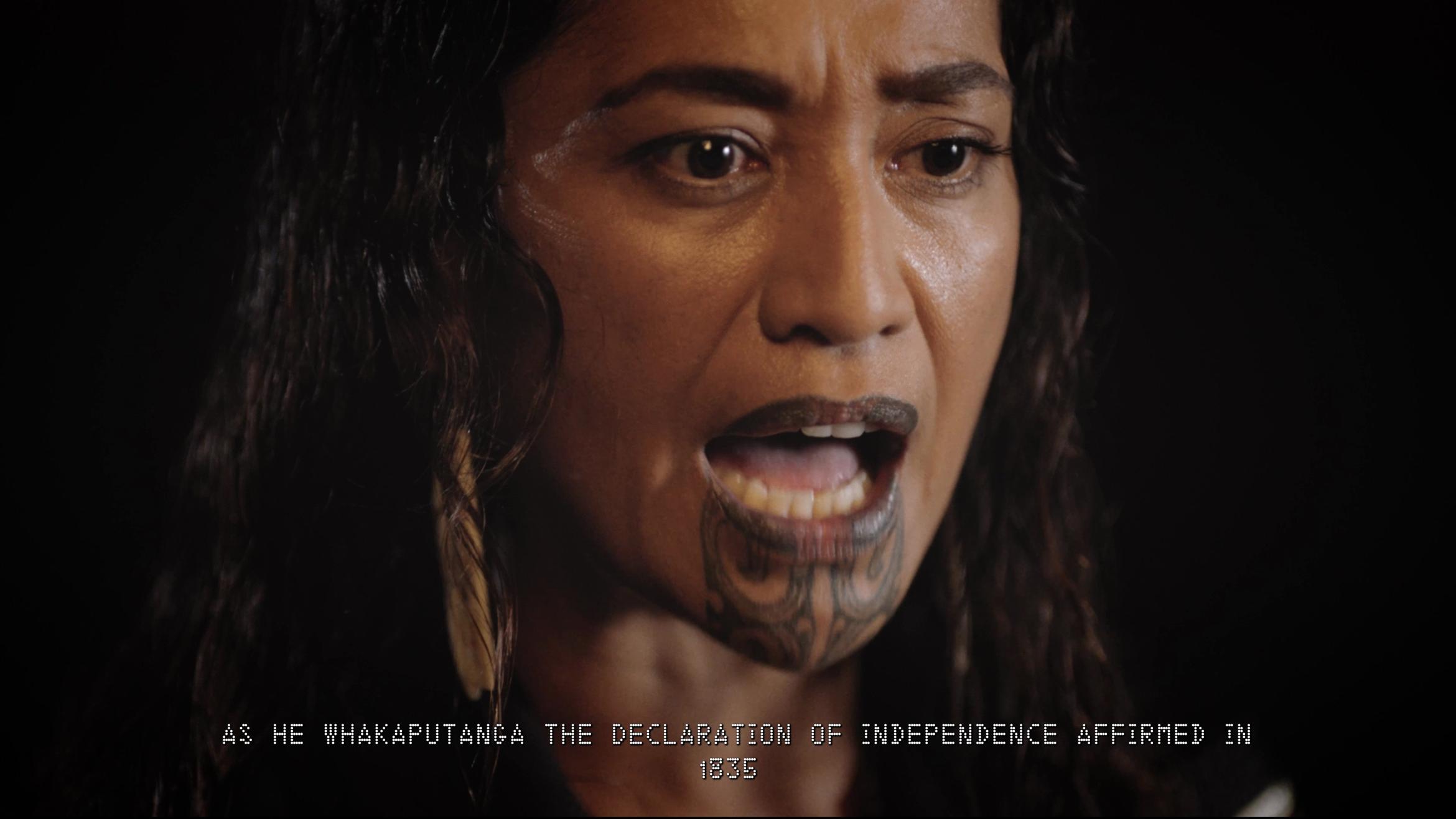 A close up of a woman with her mouth open as if speaking. Her gaze is fixed and serious. The text on the bottom of the screen says "As He Whakaputanga the Declaration of Independence Affirmed in 1835".