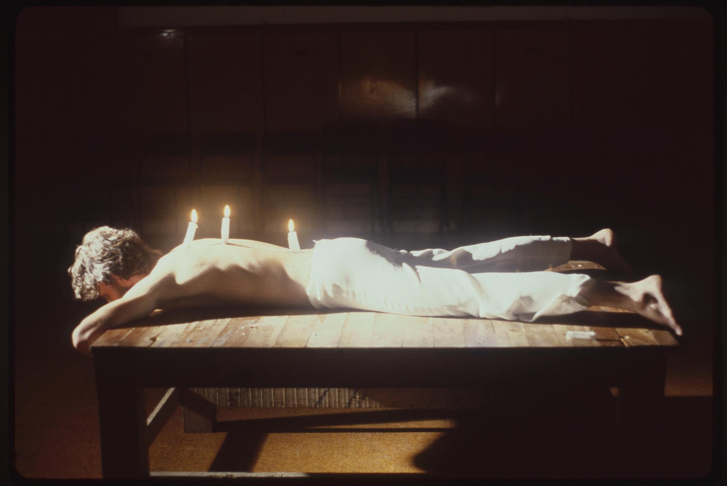 A man lies on a table with three burning candles mounted on his back