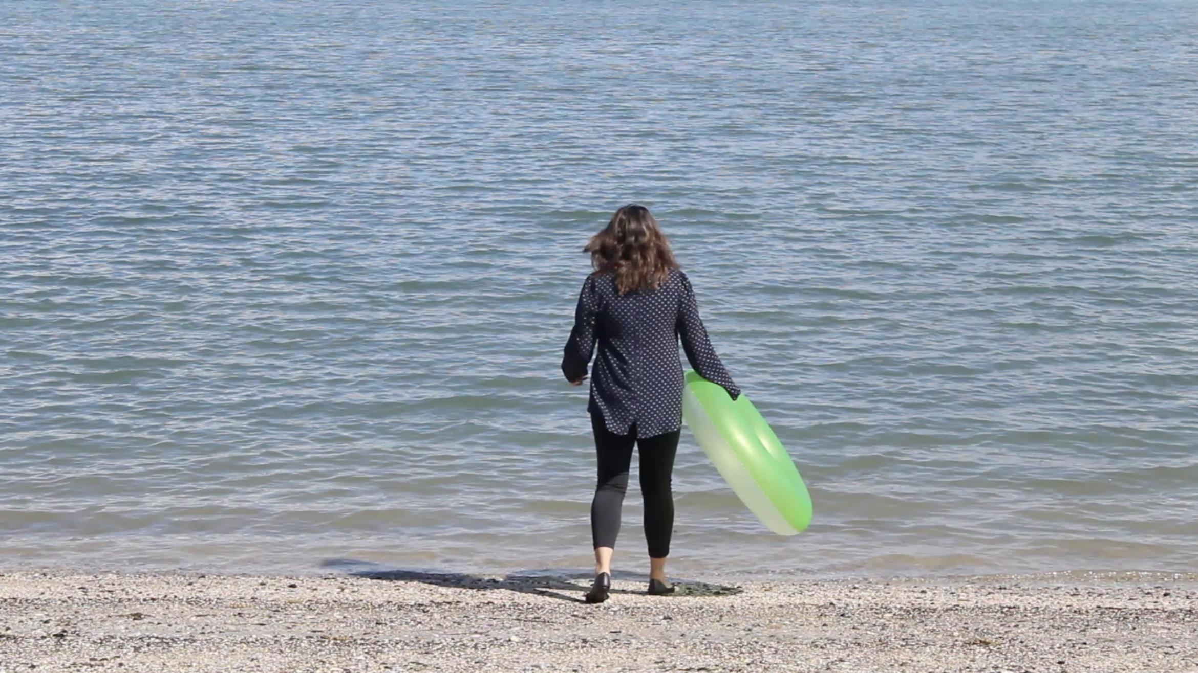 A person in retail working clothes holding an inflatable ring and walks towards the ocean.