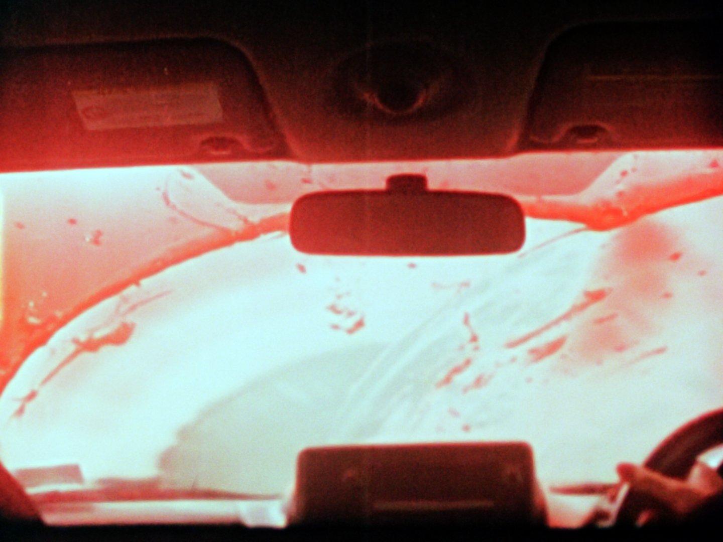 Red liquid or blood is wiped from a car windscreen, seen from inside the car