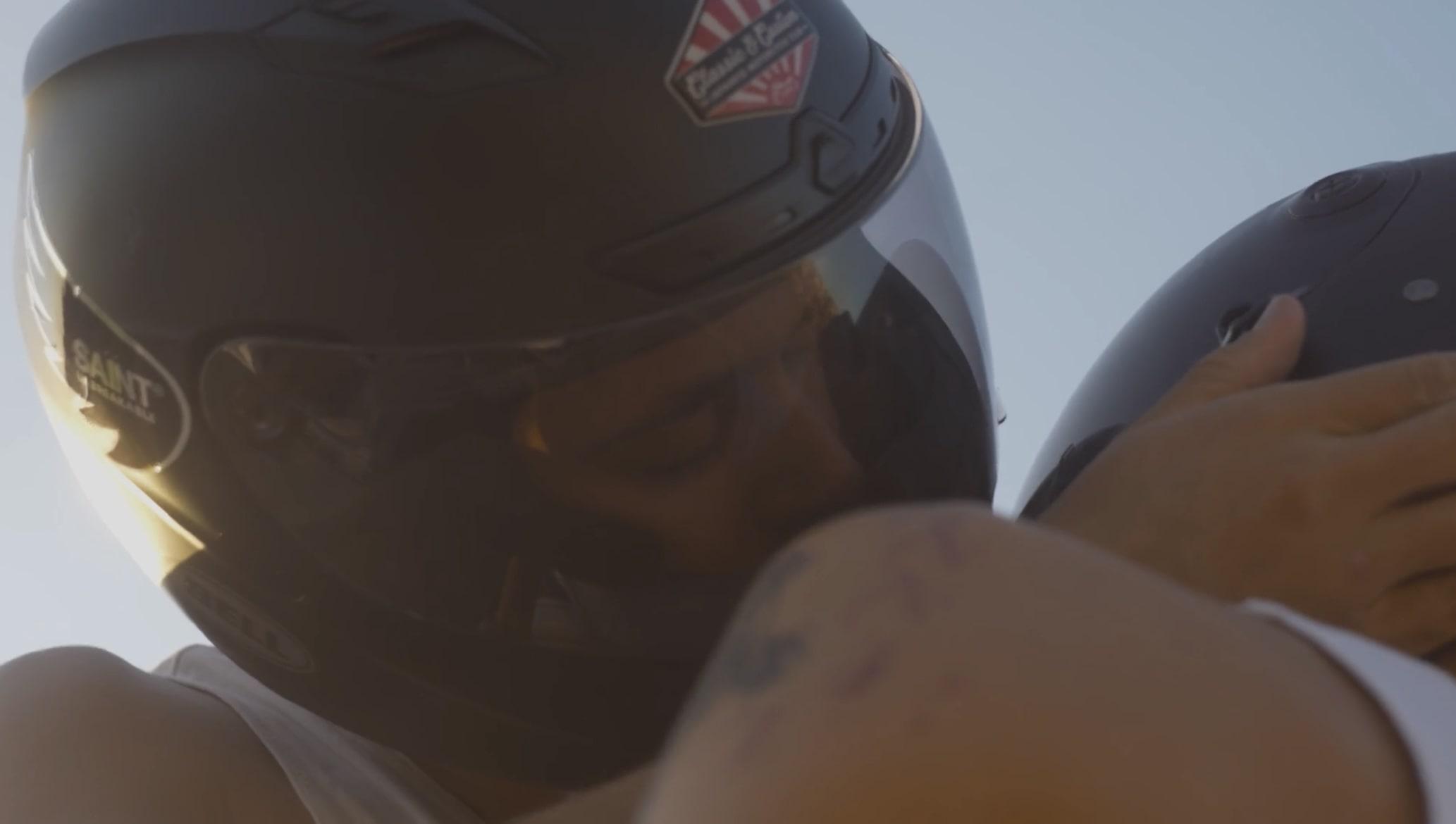 Two people in motorbike helmets appear to kiss