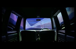 In the back seat of a CGI car, a purple digital streetscape passes by outside.