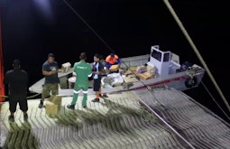 A group of people unload boxes from a small boat at night.