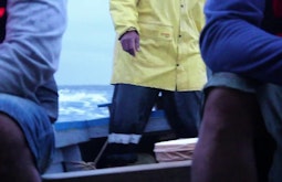 The legs and torso's of people in heavy coats while on a small boat at sea.