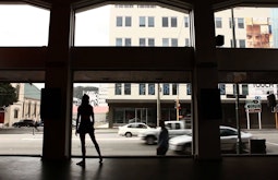 A person dances in the street facing windows of a large foyer.