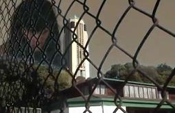 A persons head is superimposed to tower above a war memorial, there is a wire fence in front.