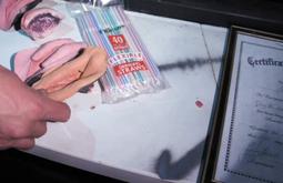 A person handles anatomical sculptures of fingers and genetalia on a plastic table.