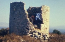 A person climbs inside an old rock fort, a blue shirt hangs on the edge.